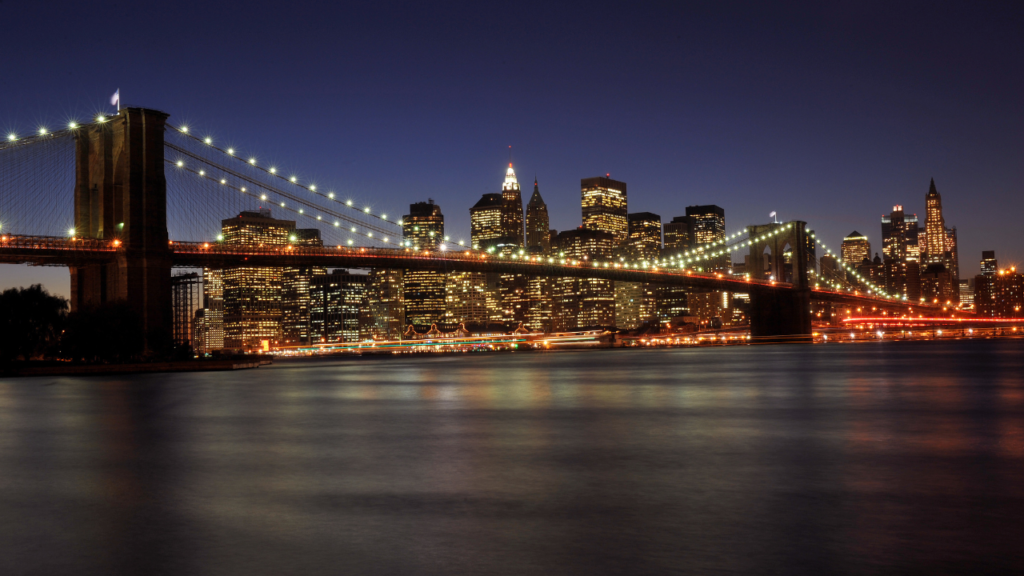 Vista panorâmica de uma cidade iluminada à noite, com ruas movimentadas e prédios reluzindo sob as luzes urbanas. Escapadas.